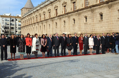 Los integrantes del Gobierno andaluz, colocados por orden protocolario, escuchan el himno de Andalucía en la fachada principal del Parlamento, tras la izada de bandera.