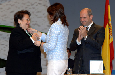 La presidenta del Parlamento de Andalucía, María del Mar Moreno, coloca la medalla de Andalucía a la empresaria onubense, Isabel Arcos Dabrio, primera mujer que dirigió una Cámara de Comercio.