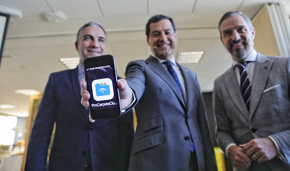 El presidente Juanma Moreno, flanqueado por Elías Bendodo y Juan Bravo, con la app Carpeta Ciudadana en su móvil.