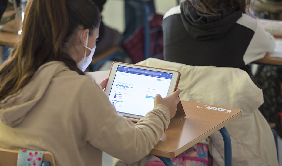 Una estudiante con mascarilla utilizando un portátil en un aula.