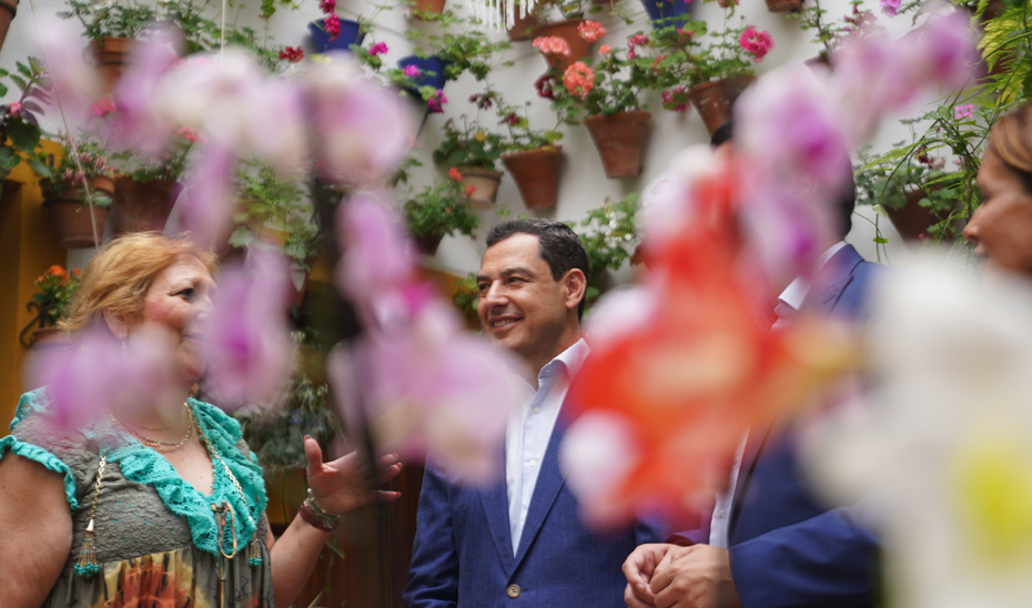 Juanma Moreno, junto a una vecina, rodeados por las flores de un patio cordobés.