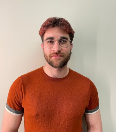 Plano medio corto de Sergio R. Suárez. Hombre con camiseta color caldera, barba y gafas sobre fondo de color blanco crudo