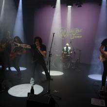 Una banda de rock en un escenario iluminado por luces de proyector.