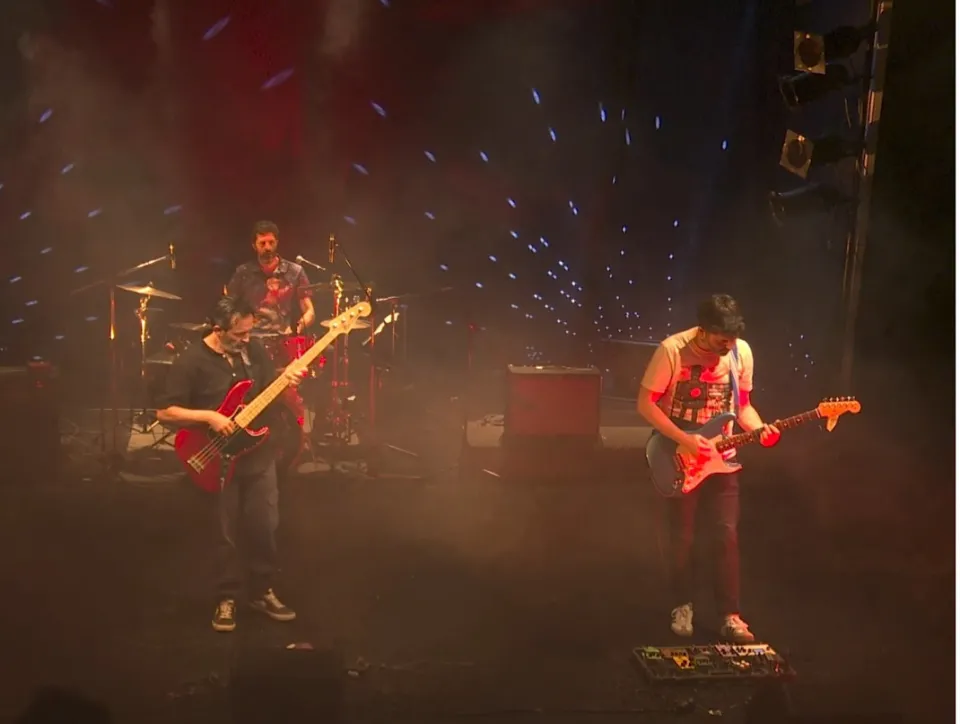 Una banda de rock tocando en un escenario oscuro y brillante iluminado.