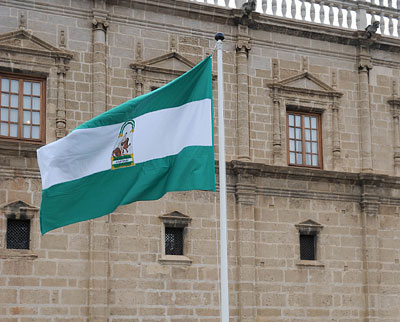 La bandera blanca y verde ondea al viento frente a la puerta principal del Parlamento de Andalucía, durante el acto de homenaje a la insignia.