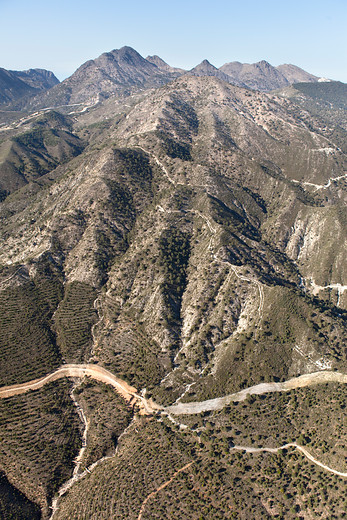 Primer plano de paisaje montañoso atravesado por caminos y un cortafuego, con poca vegetación y una zona de reforestación.