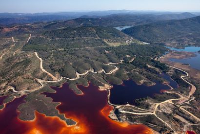Vista aerea de Río Tinto: paisaje de la sierra dividida por caminos y cortafuegos donde se aprecia una masa de agua de color anaranjado.