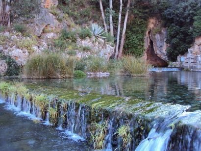 Ampliar imagen: Fotografía de un río con un salto de agua en forma de escalón no natural y pared de rocas con vegetación