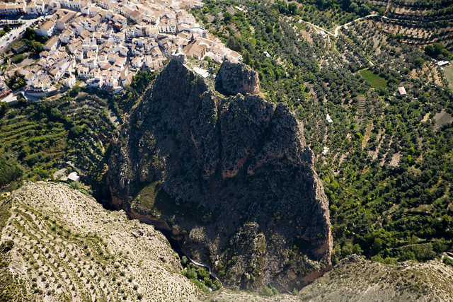 Fotografía aérea de una gran montaña rocosa en el centro de la imágen. En la parte superior se puede ver el pubelo de Castril con casa blancas y el resto de la imagen árboles y terrenos de cultivo