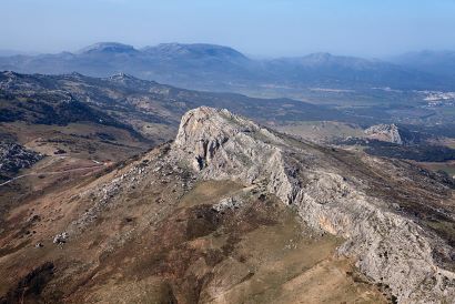 Fotografía aerea de montaña, en primer plano un gran tajo y al fondo mas montañas y una población.