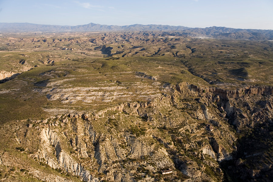 Ampliar imagen: vista aerea del Paraje Natural Karst en Yesos de Sorbas. En la parte derecha se observa como el terreno se encuentra fracuturado por el barranco del Tesoro. Paisaje dominado por la aridez y la escasa vegetación. Al fondo la sierra de Filabres y en un plano de media distancia se observa un paisaje dominado por las cárcavas.