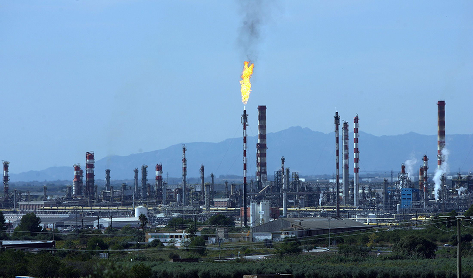 Instalación de refinería con muchas tuberías y humo visible en el aire.