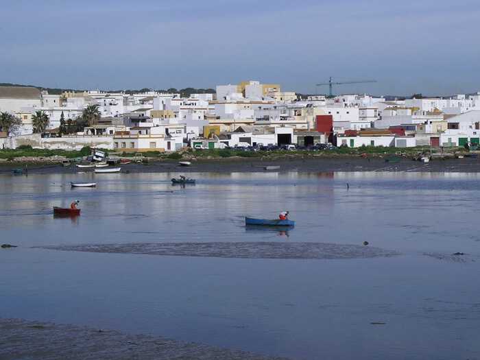 Pueblo costero de casas blancas junto al agua baja, con pescadores en pequeños botes