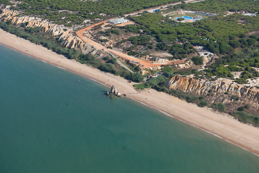 Ampliar imagen: Foto de un acantilado a pie de playa que cruza en diagonal la fotografía donde se puede apreciar el más por un lado del acantilado y vegetación por el otro lado del mismo.