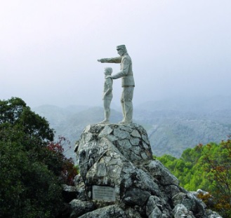 Estatua de un guarda forestal, apoyando su mano sobre el hombro de un niño, mientras que con la otra, señala el paisaje