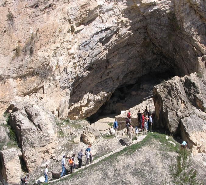 Foto de una cueva con una fila de personas recorriendo el camino que conduce a la abertura de la misma