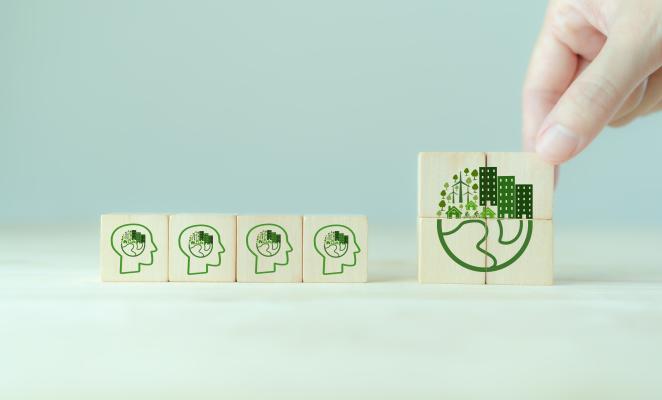 Cubos de madera con iconos de mentes ecológicas y una mano formando una imagen de ciudad sostenible