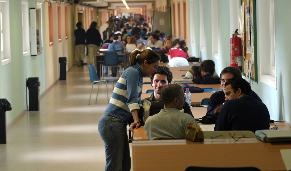 Universitarios andaluces en el pasillo de una facultad con mesas habilitadas para trabajos en grupo.