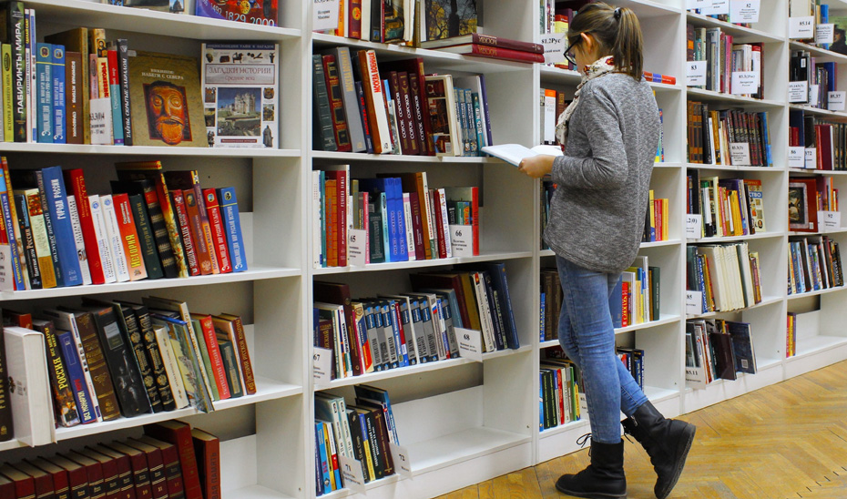 Una chica ojea un libro en una biblioteca.