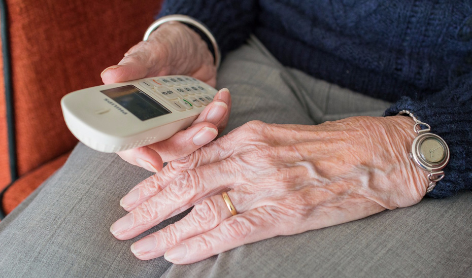 Las manos de una persona de avanzada edad sosteniendo un teléfono.