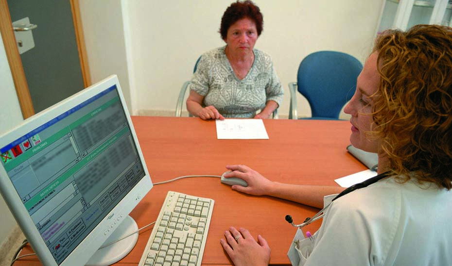 Una doctora consulta el historial clínico de una paciente en el ordenador de su consulta.