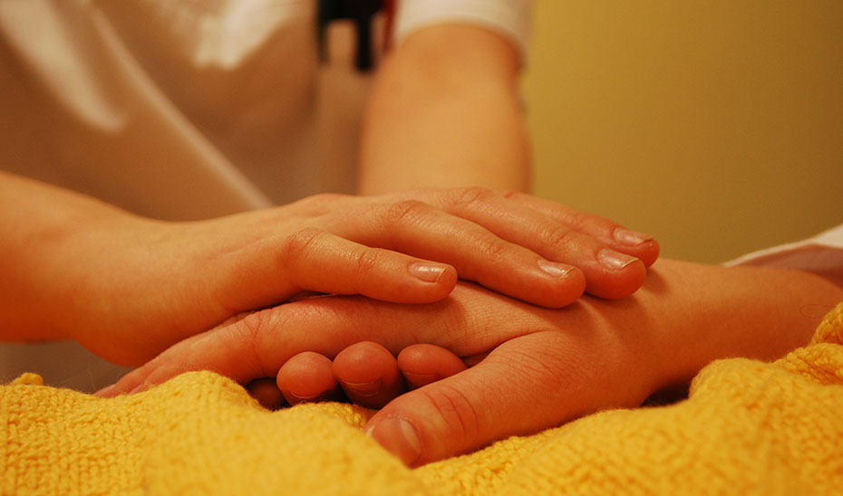 Una profesional da la mano a un paciente en cuidados paliativos.