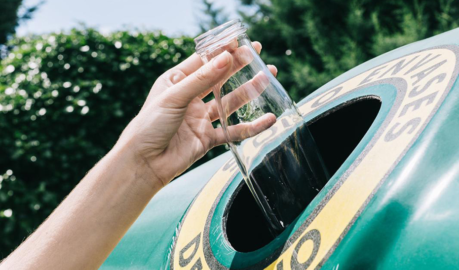 Una persona deposita una botella de vidrio en un contenedor.