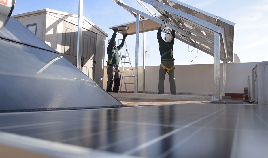 Dos operarios proceden a la instalación de placas solares para autoconsumo energético en un edificio.