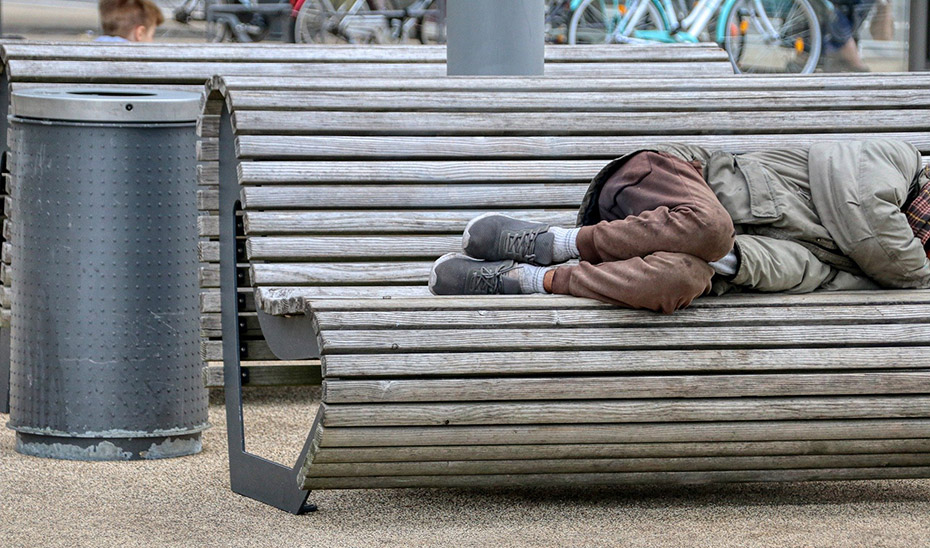 Una persona sin hogar durmiendo en un banco de un parque.