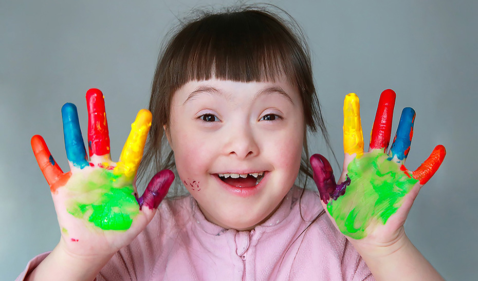 
			      Una niña con síndrome de Down juega pintando sus manos de colores.			    
			  