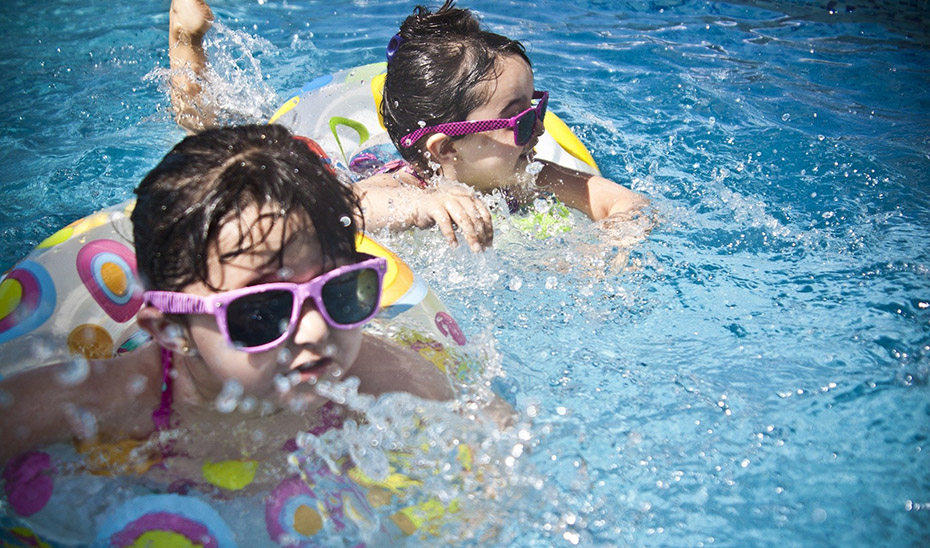 Dos niños equipados con flotadores y gafas de sol juegan en una piscina.