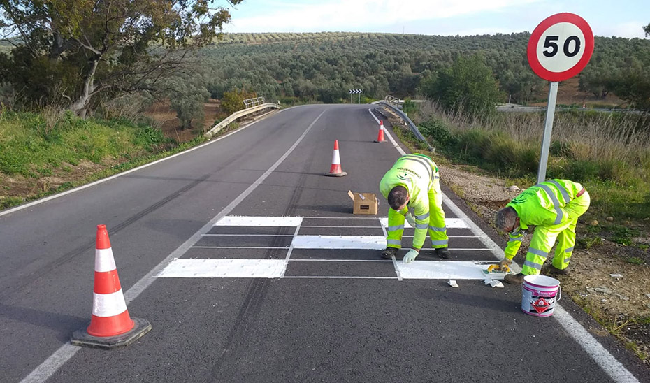 Dos trabajadores pintan señales viarias en una carretera andaluza.