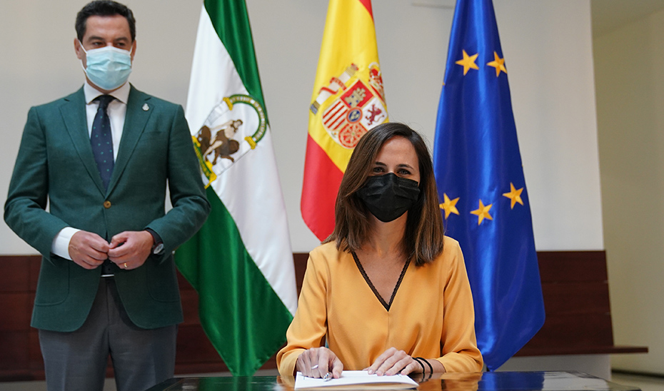 El presidente Juanma Moreno observa a la ministra Ione Belarra mientras rubrica el documento. 