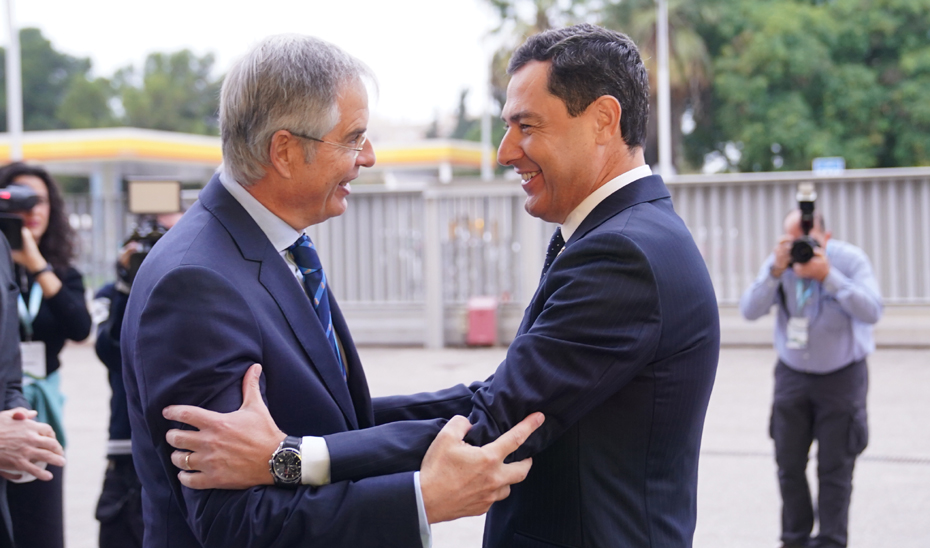 Juanma Moreno saluda al presidente del Real Automóvil Club de España (RACE), Carmelo Sanz, a su llegada al acto.
