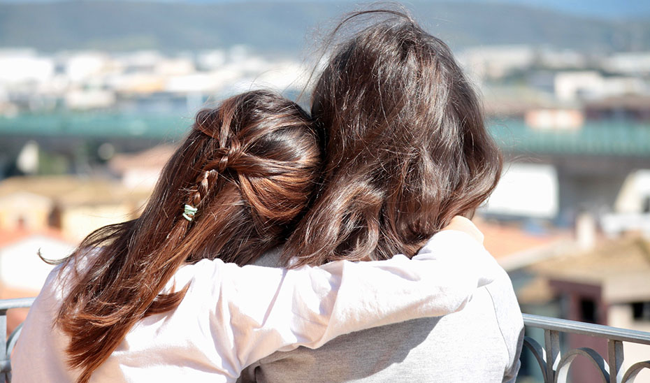 Dos mujeres se abrazan con la mirada puesta en el horizonte.