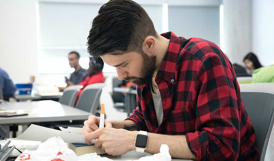
			      Estudiante universitario en un aula.			    
			  