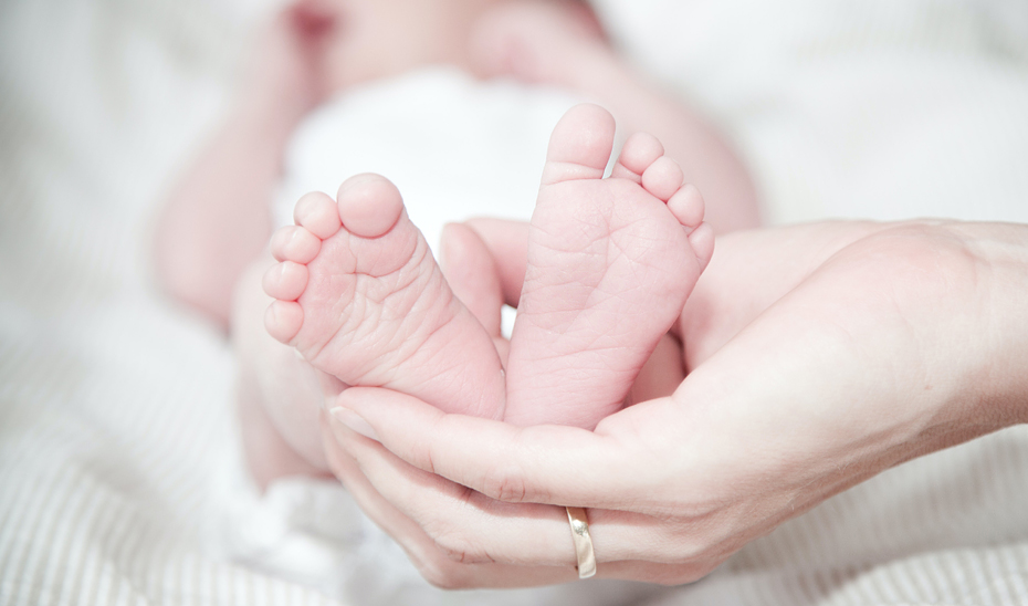 Las manos de una madre sostienen los pies de su bebé.