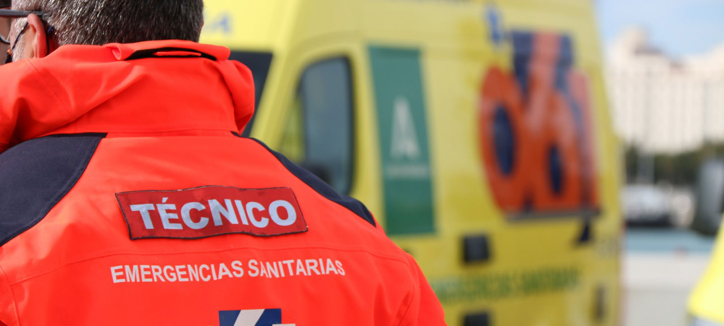 Espalda de un trabajador el Instituto de Emergencias, con su uniforme y una ambulancia de fondo